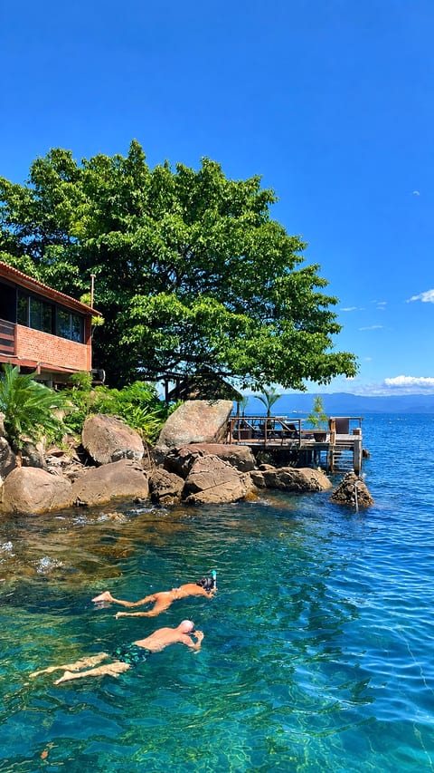 Hóspedes fazendo snorkel na água transparente em frente às pedras da Pousada Convés, em Araçatiba